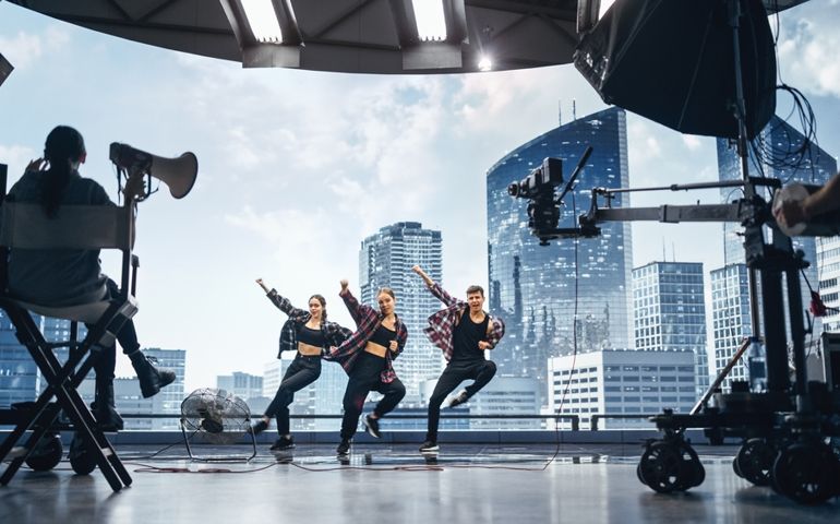Music Clip Studio Set: Shooting Hip Hop Video Dance Scene with Three Professionals Dancers Performing on Stage with Big Led Screen with Modern City Background. Director and Cameraman in Backstage.