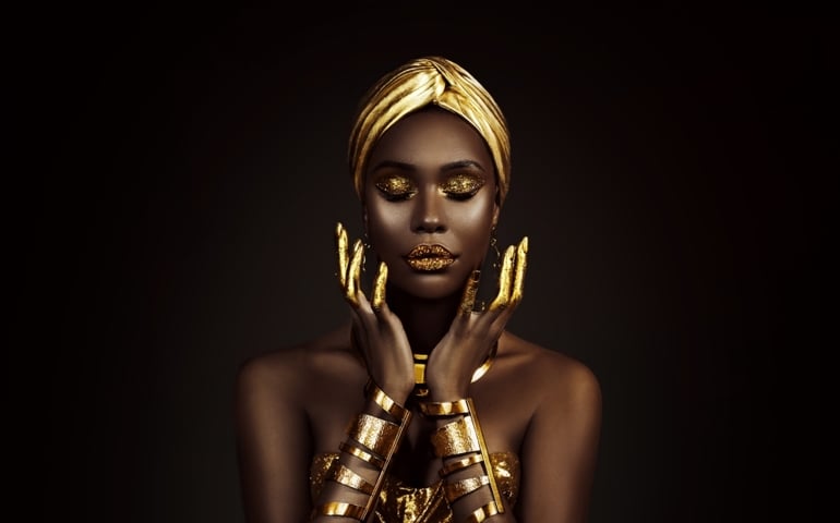 Portrait closeup Beauty fantasy african woman face in gold paint. Golden shiny skin. Fashion model girl goddess hand fingers posing. Arab turban head, jewellery bracelets. Professional metallic makeup