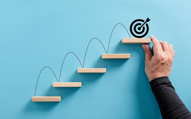 Male hand arranges a wooden block staircase with target icon. Achieving goals and objectives or goal setting concept.