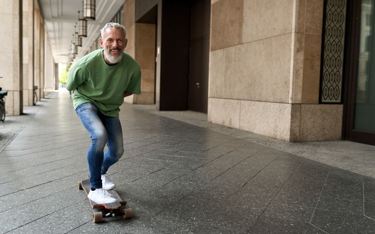 Active energetic happy cool gray haired old adult man skateboarding on city street, smiling sporty fit middle aged mature older male professional skater having fun enjoying riding skateboard outdoor.