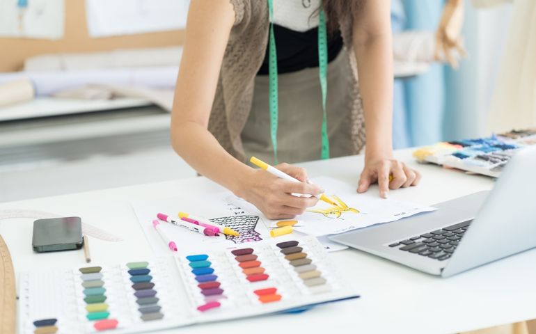 Female dressmaker or hands of fashion designer drawing sketches model on paper for clothes in atelier in tailor shop. Fashion, dressmaking concept