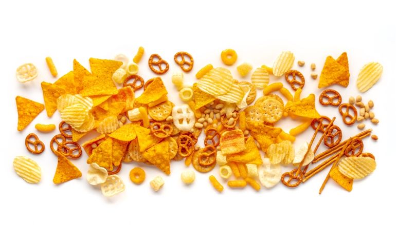 Salty snacks texture on a white background. Party food mix. Potato and tortilla chips, crackers and other appetizers, overhead flat lay shot
