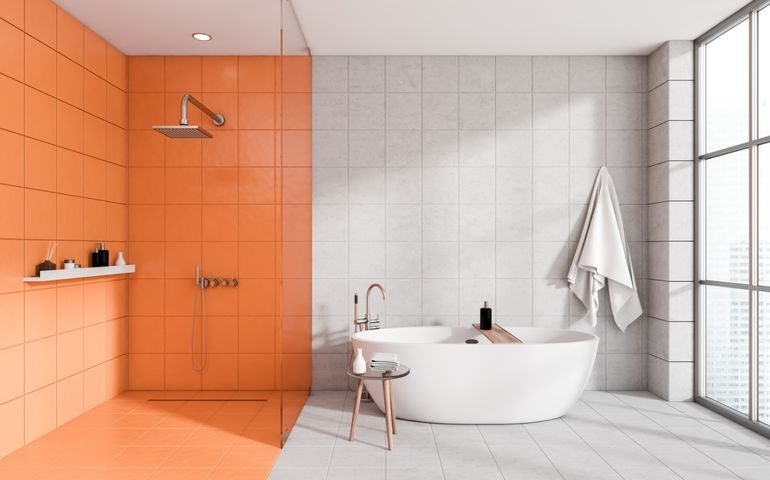 Front view on bright bathroom interior with bathtub, shower, white and orange walls, panoramic window with city skyscrapers view, concrete tile floor, glass partition, stool with towel
