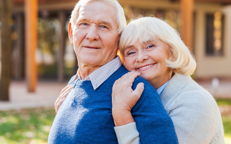Feeling safe near him. Happy senior couple bonding to each other and smiling while standing outdoors and in front of their house