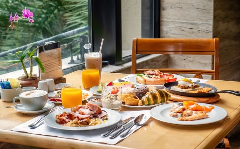 Breakfast in luxury hotel. Table full of various food from buffet in modern resort. Morning food - fresh bakery, glasses of orange juice, eggs, cold cuts and plate with tropical fruits in restaurant