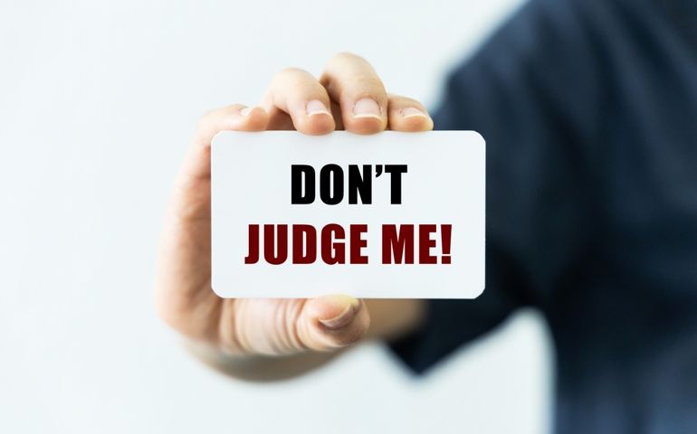 Don't judge me text on blank business card being held by a woman's hand with blurred background. Business concept to inform others don't judge me.