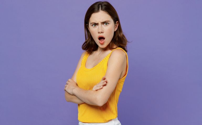 Side view young sad angry indignant woman 20s she wear yellow tank shirt hold hands crossed folded look camera isolated on plain pastel light purple background studio portrait People lifestyle concept