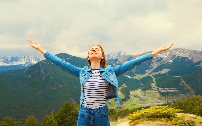 Travel concept, happy woman enjoying fresh air mountains raising her hands up on Andorra mountain background