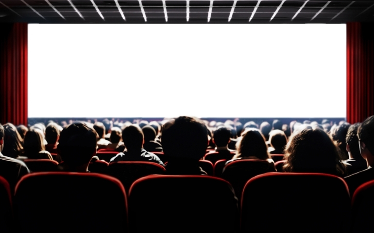Cinema blank wide screen and people in red chairs in the cinema hall. Blurred People silhouettes watching movie performance.