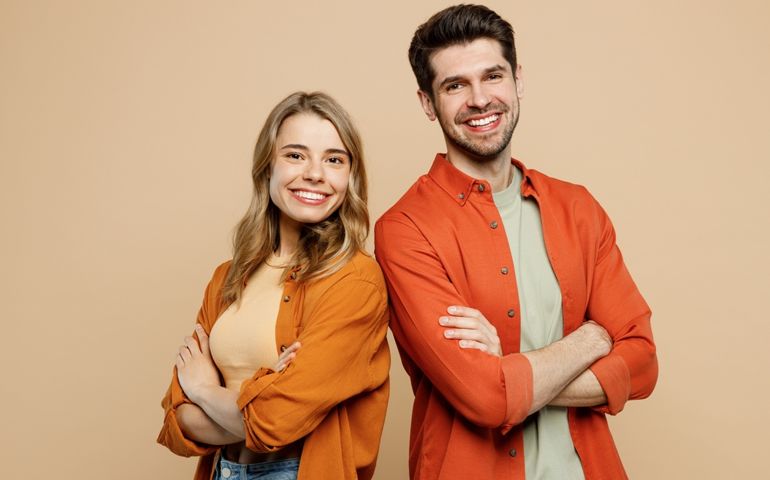 Side view young smiling happy fun cool couple two friends family man woman wear casual clothes hold hands crossed folded together isolated on pastel plain light beige color background studio portrait
