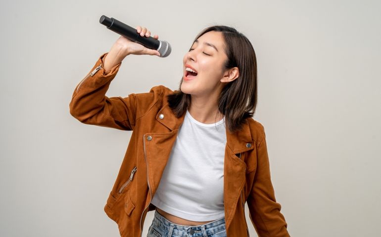 Happiness young asian woman singing song. Artist vocalist singer on isolated background. Confident woman public speaking talking with microphone in studio.