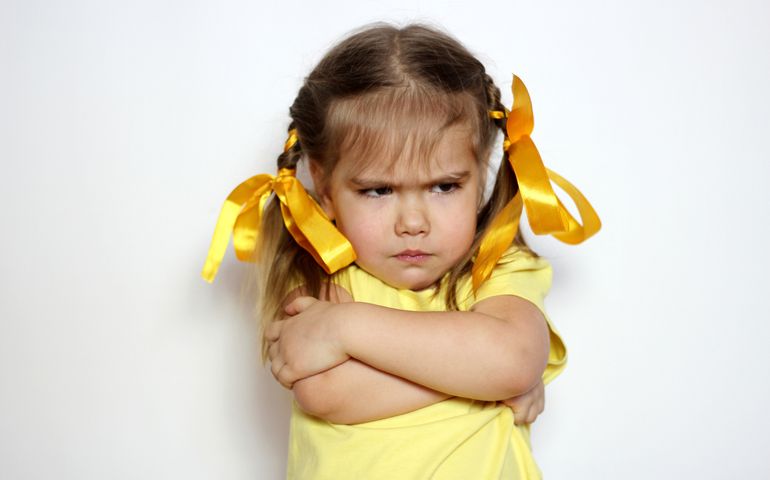 Angry little girl with yellow bows and yellow T-shirt over white background, sign and gesture concept
