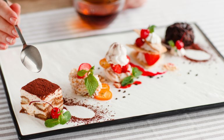 Tasting one cake from lots, close-up. Plate with five different sweet desserts, hand taking one. Degustation, choosing dessert for party or wedding, gastronomy, event organization concept