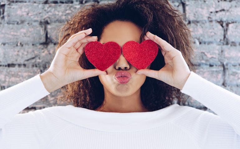 Valentine Day Love Beautiful concept . Happy African American girl holding two hearts on her eyes.