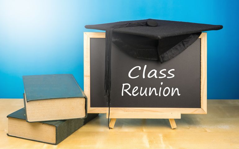 Graduation hat, books, blackboard with text class reunion on a wooden background.