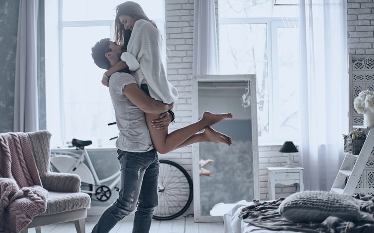 Expressing their love. Handsome man in white T-shirt carrying young attractive woman while spending free time at home