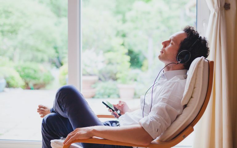 listening relaxing music at home, relaxed man in headphones sitting in deck chair in modern bright interior