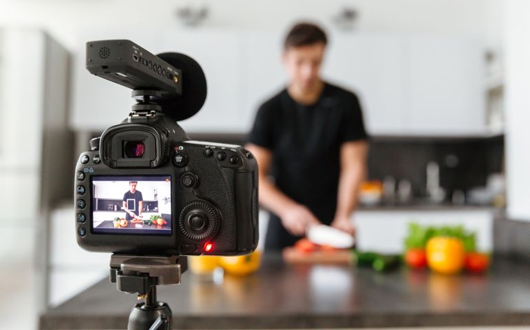 Close up of a video camera filming young male blogger at the kitchen