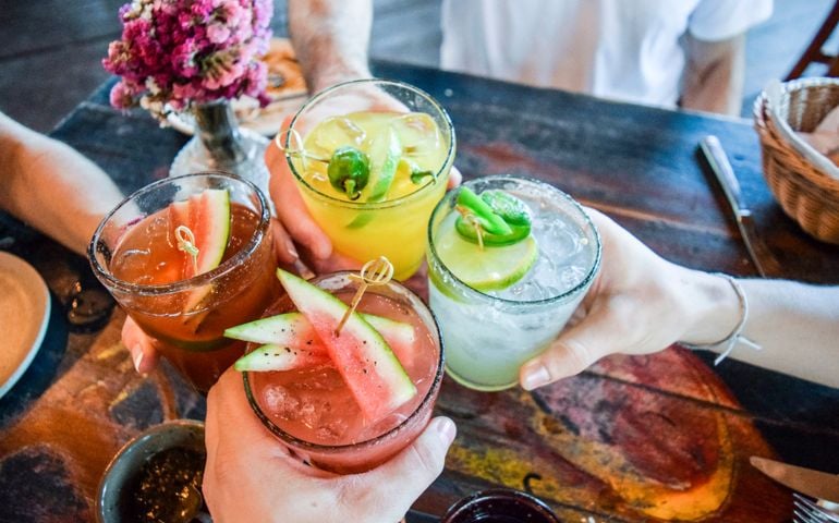 Friends toasting, saying cheers holding tropical blended fruit margaritas. Watermelon and passionfruit drinks.