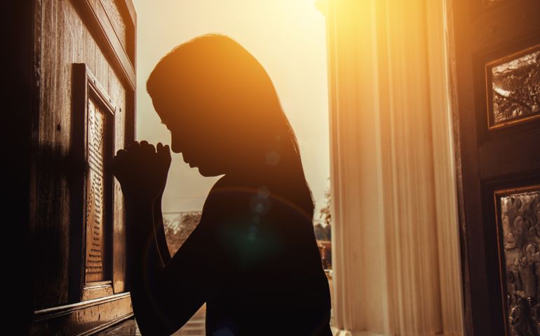 silhouette of woman kneeling and praying in modern church at sunset time