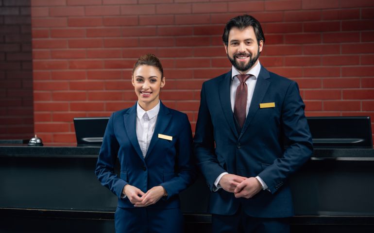 hotel receptionists standing together in front of counter and looking at camera