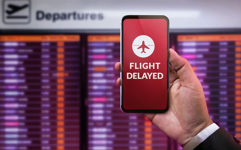 Modern Technology in Travel Concept. Flight Delayed on Smartphone Screen. Businessman using Mobile Phone in front of Departures Board to Re-Checked Flight Information in Airport
