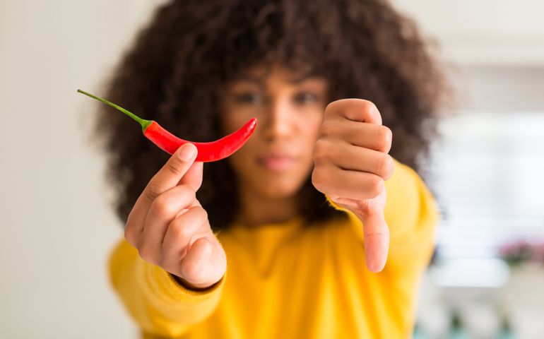 African american woman eating red hot chili pepper with angry face, negative sign showing dislike with thumbs down, rejection concept