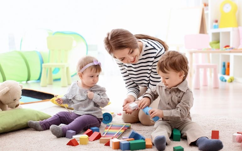 Young nanny playing with little children, indoors