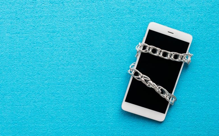 White smartphone with metal chain on blue background. Digital detox, dependency on tech, no gadget and devices concept