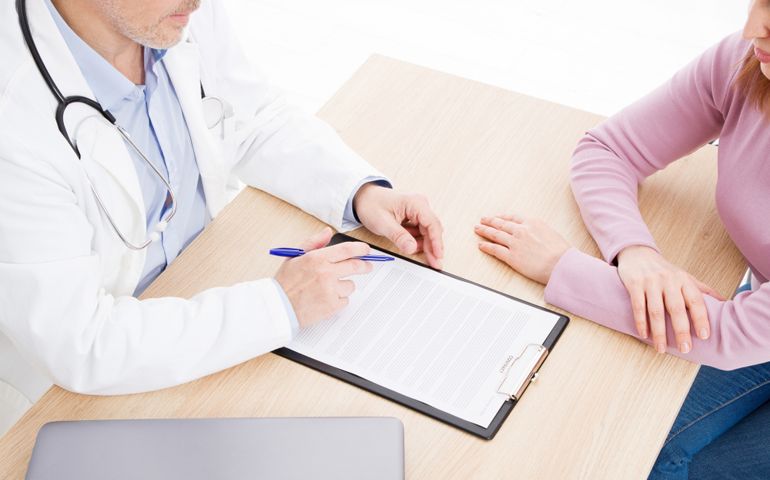 Patient listening intently to a male doctor explaining patient symptoms or asking a question as they discuss paperwork together in a consultation