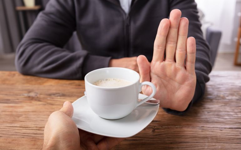 Close-up Of A Man's Hand Refusing Cup Of Coffee Offered By Person Over Wooden Desk
