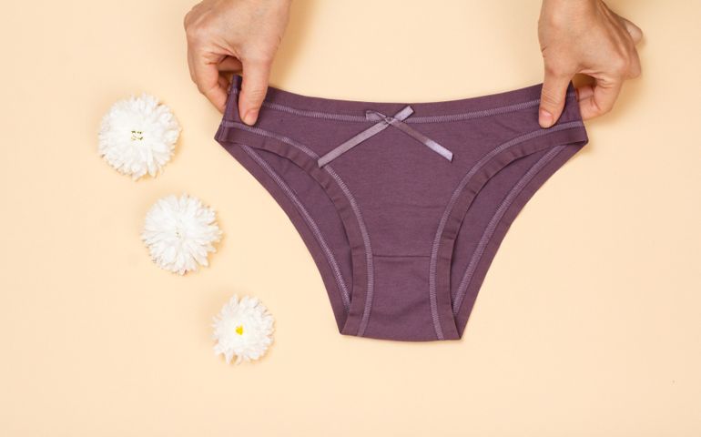 Women's hands holding beautiful cotton brown panties on beige background. Woman underwear set. Top view.