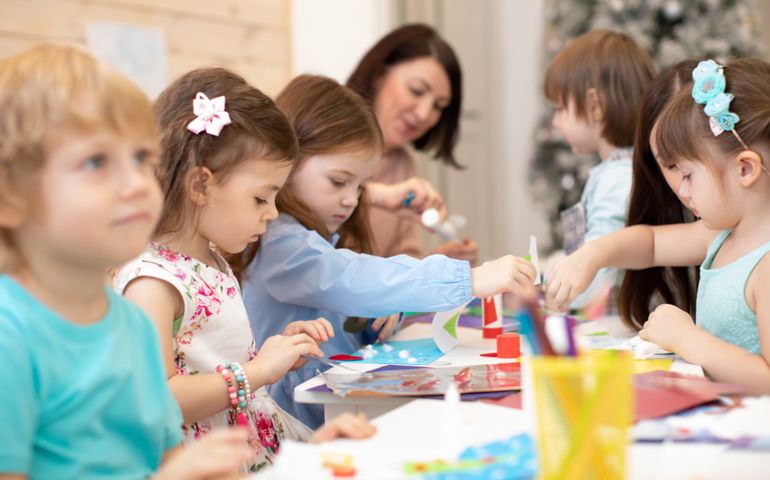 Group of children on hand arts lesson in kindergarten. Teacher helps kids hands working. Preschool students activities in class