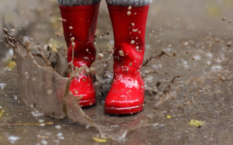 Child Wearing Red Rain Boots Jumping Into A Puddle