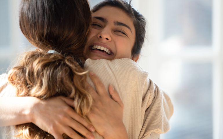 Head shot close up happy mixed race girl cuddling smiling indian female friend. Overjoyed excited best buddies emracing hugging, greeting each other with success, true strong friendship concept.