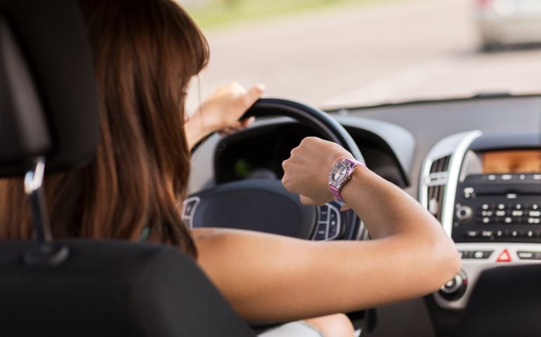 transportation and vehicle concept - woman driving a car and looking at watch