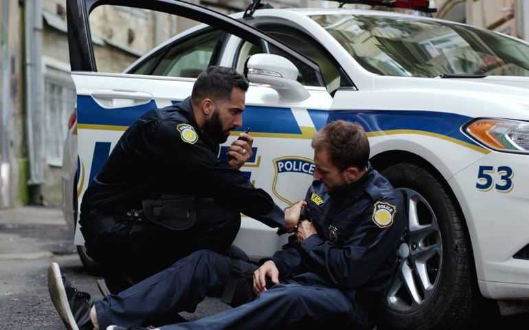 oor brave policeman was shoot in the shootout leaning on the police car. His colleague aiming a gun following criminals trying