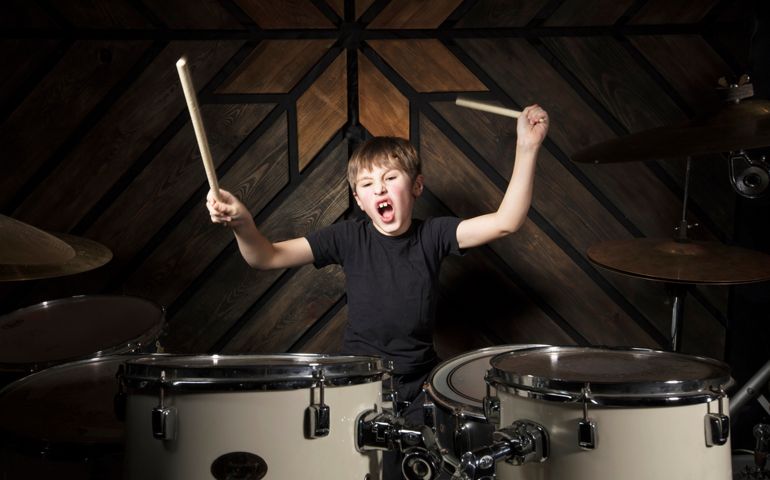 The child plays the drums. Boy musician behind a drum kit.