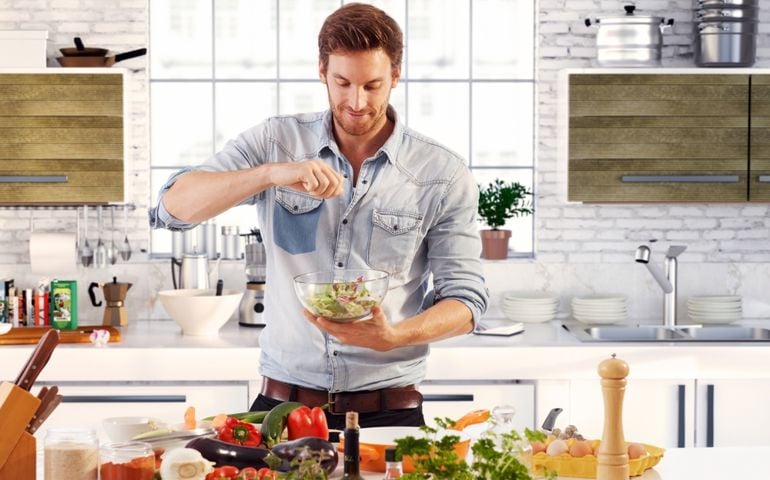 Handsome man cooking at home preparing salad in kitchen.