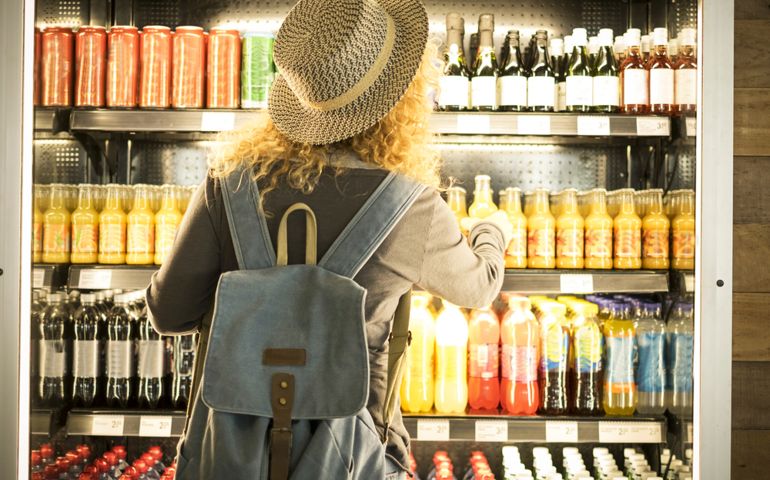 Travel woman viewed from back choosinf beverage in a fresh fridge - airport or station bar concept and traveler passenger choosing drinks - modern lifestyle backpack people buying drinks bottles
