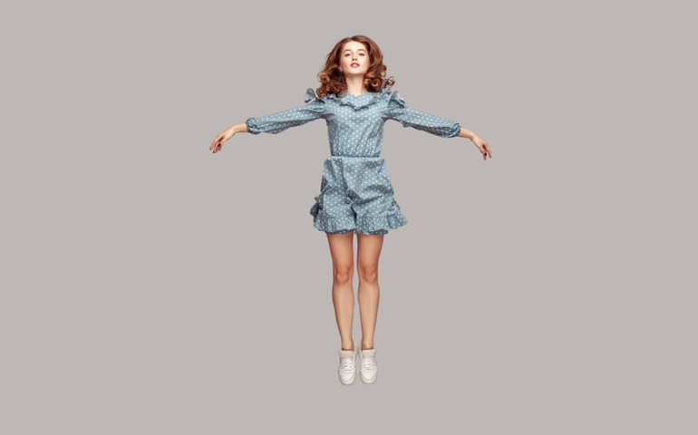 Full length happy calm pretty girl in vintage ruffle dress levitating hovering in mid-air with raised hands as wings, jumping trampoline or flying up. indoor studio shot isolated on gray background