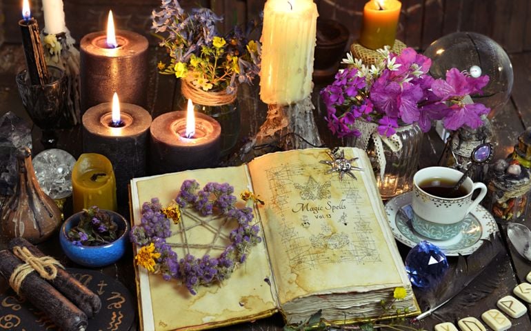 Open witch book with spells, black candles and cup of coffee.