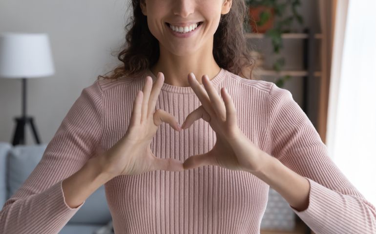 Close up cropped image smiling young woman showing heart love sign with fingers, feeling grateful indoors. Sincere happy millennial female volunteer expressing support and kindness, charity concept.
