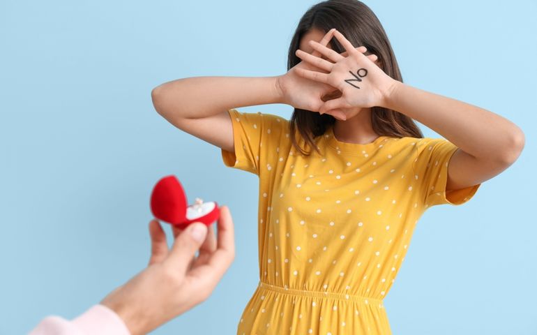 Young woman rejecting marriage proposal on blue background
