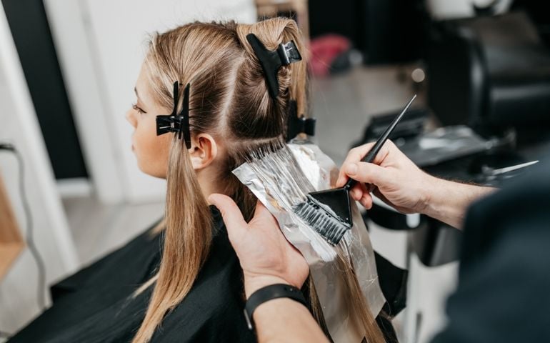 Hairdresser is applying bleaching powder on woman's hair and wrapping into the foil.
