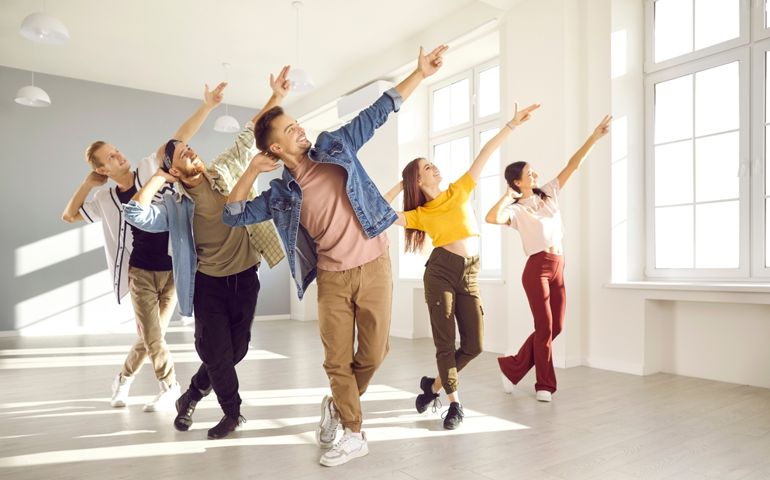 Happy energetic young hip-hop dancers dance together in bright spacious dance studio. Active young women and men in modern casual clothes pursue their hobbies and learn new dance movements
