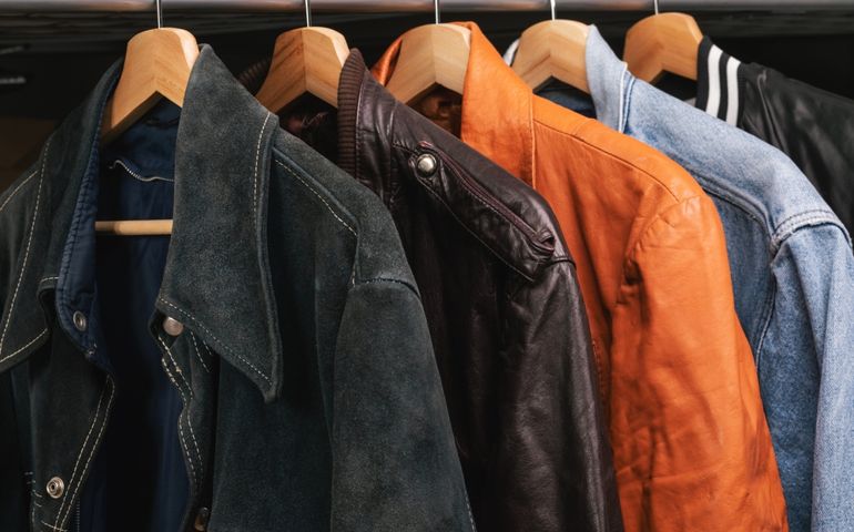 Various vintage suede leather and jeans jackets on hanger rack in a used goods store. Thrifting and sustainability in clothing concept