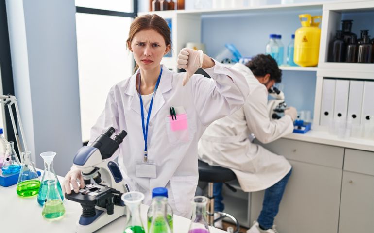 Young two people working at scientist laboratory with angry face, negative sign showing dislike with thumbs down