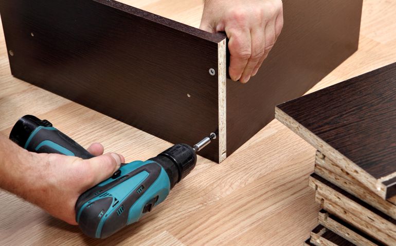 Assembling furniture from chipboard, using a cordless screwdriver, close up.
