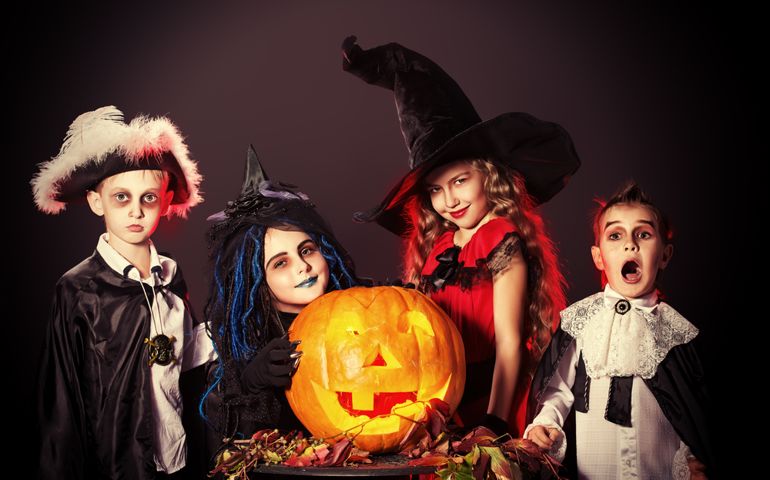 Cheerful children in halloween costumes posing with pumpkin over dark background.